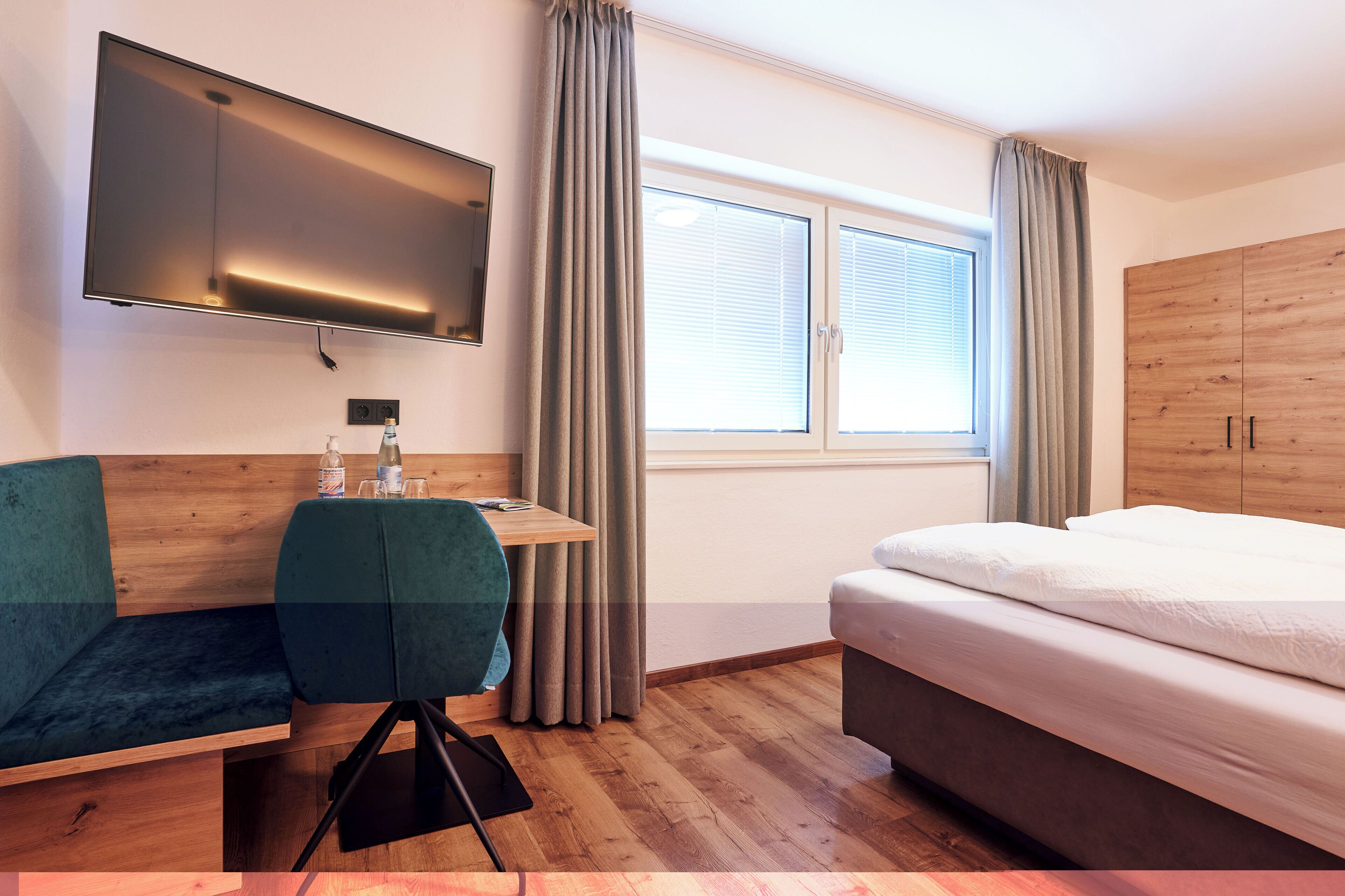 Ein Hotelzimmer mit Bett, Schreibtisch mit Stuhl, Wandfernseher und einem Fenster mit Vorhängen.