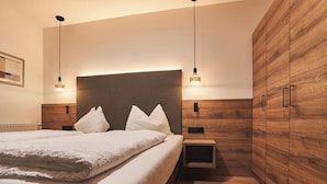 A modern bedroom with a large bed, wooden wardrobe, and bedside lamps. - Pension Sunnhofer (Terlano)