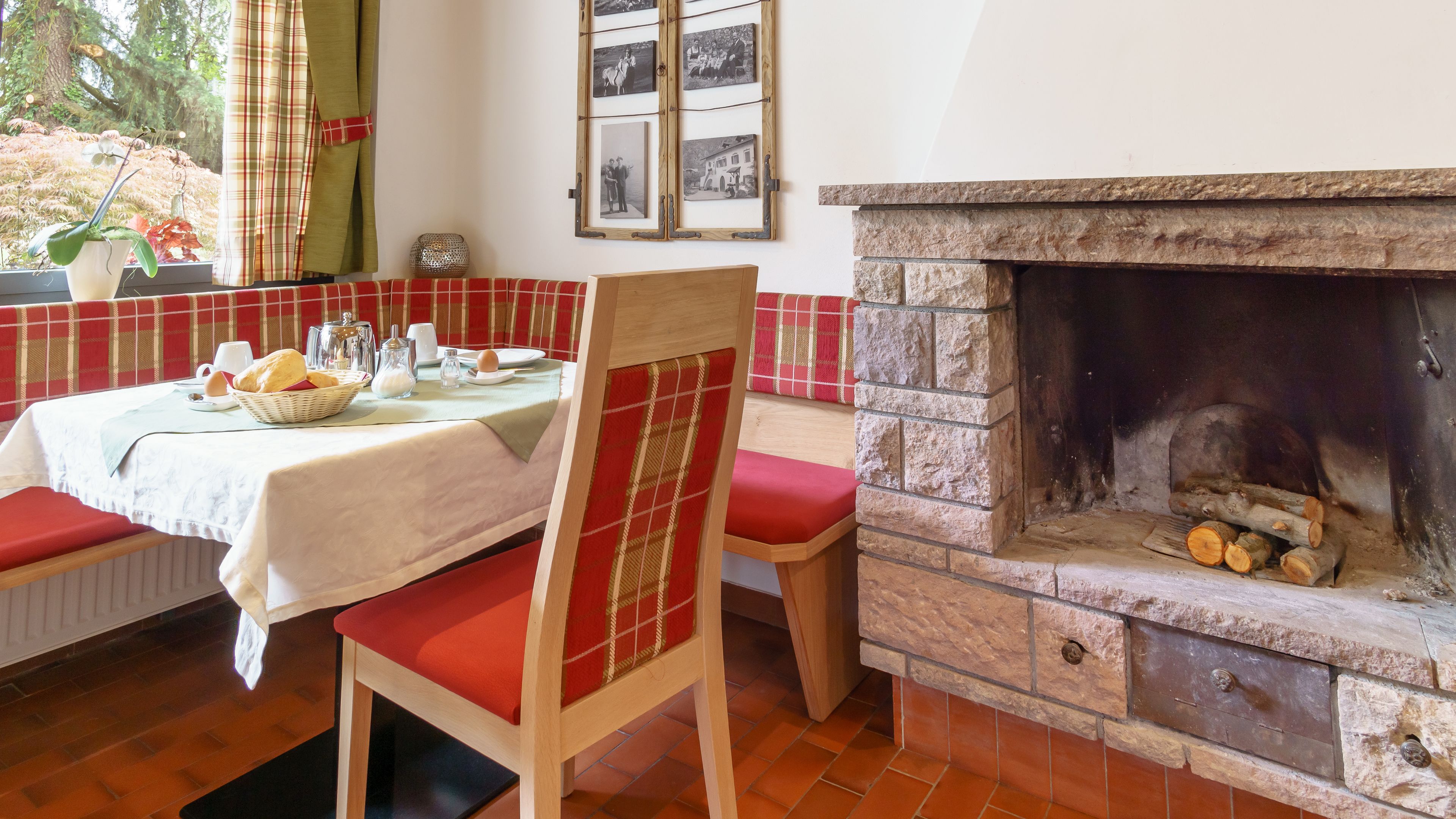 A cozy dining area with a fireplace, a table set with bread and a basket, and a chair with a red cushion.