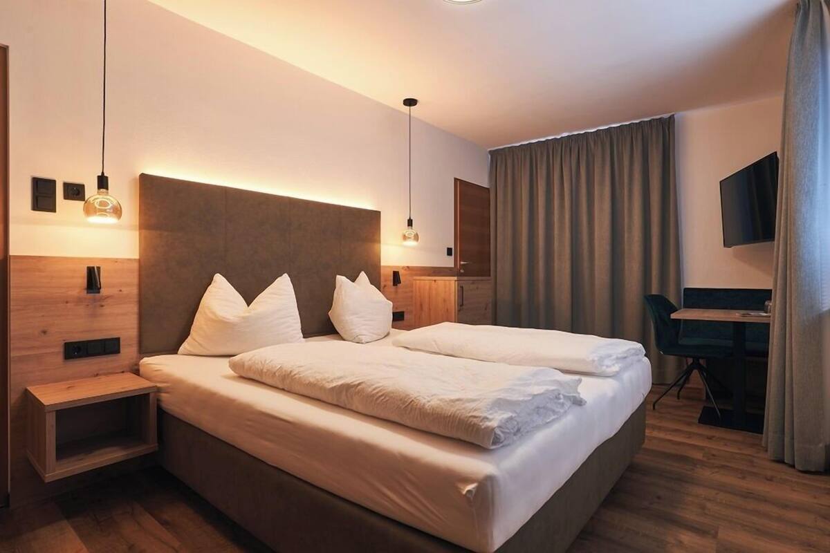 A modern hotel room with a large bed, bedside tables, a desk, and a TV.