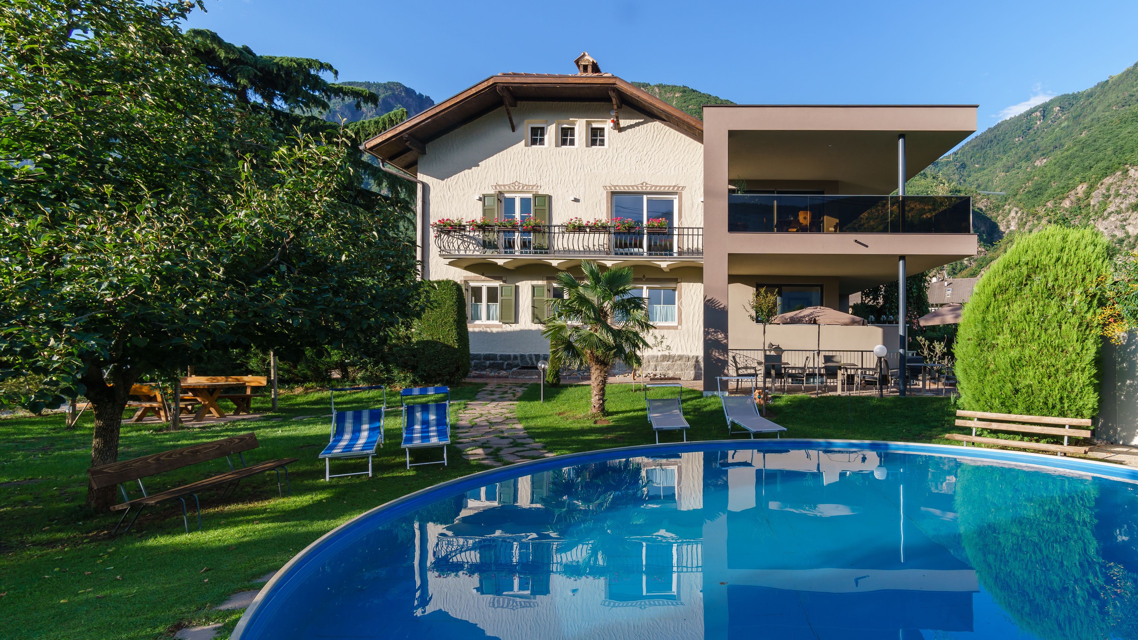 A two-story building with a pool, outdoor seating, and a mountain backdrop.