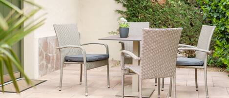 Un patio con sillas de mimbre y una mesa, rodeado de follaje.