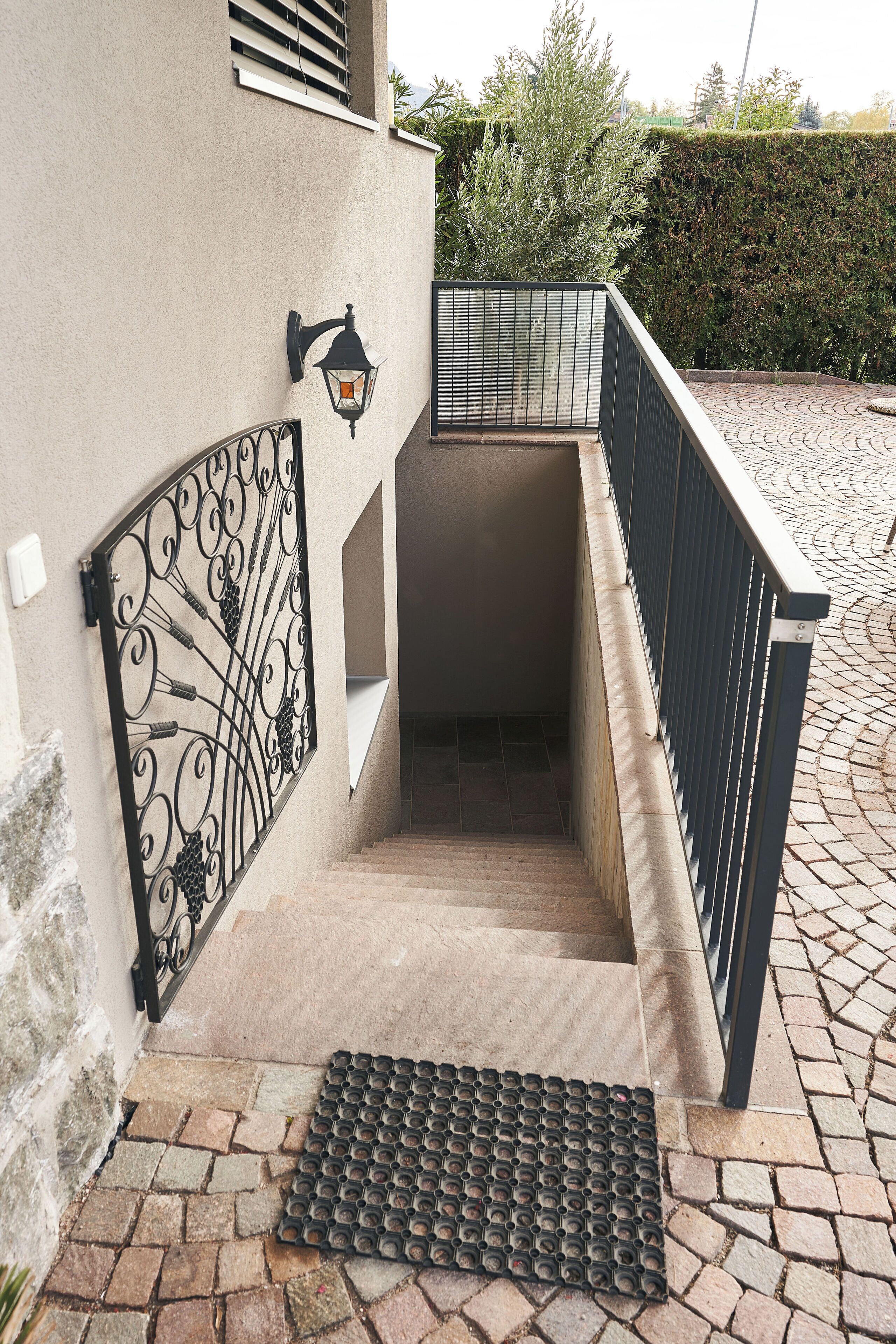 A set of outdoor stairs with a metal railing, a decorative wall-mounted light, and a metal mat at the bottom.