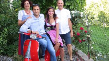 A family on a red scooter in a garden with a fence and flowers.