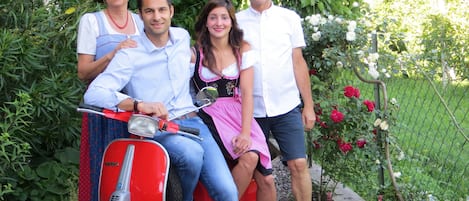 Una familia en un patinete rojo en un jardín con una valla y flores.