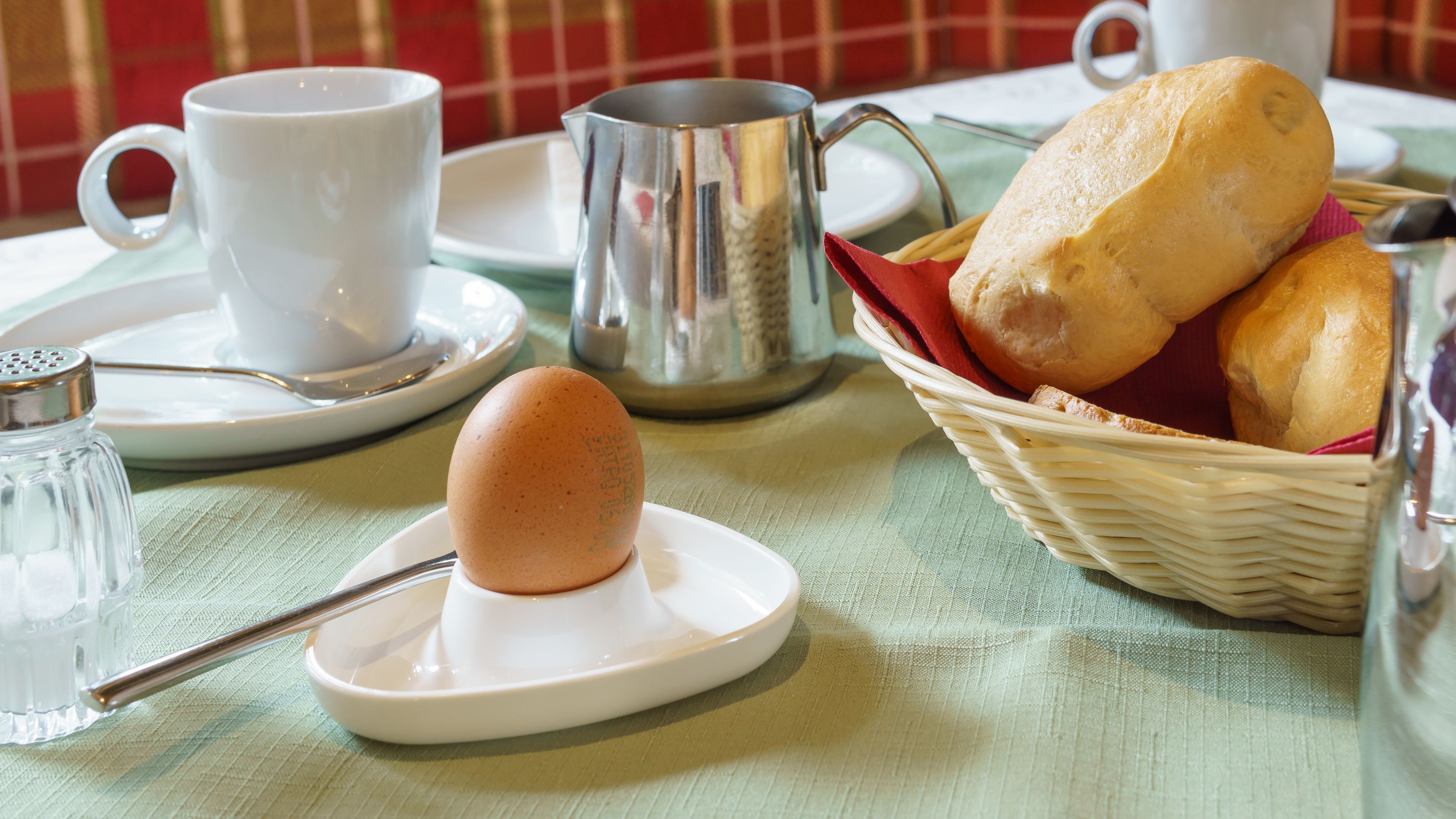 A breakfast setting with a cup, mug, salt shaker, bread, and a basket.
