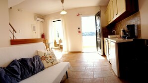 A cozy living area with a sofa, a kitchen with a coffee machine, and a view through an open door. - Agios Nikitas View (Lefkada)