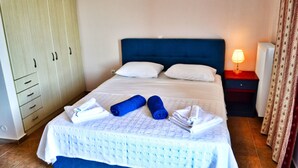 A neatly made bed with white linens and blue towels, a blue headboard, a bedside table with a lamp, and a wardrobe with multiple doors. - Agios Nikitas View (Lefkada)