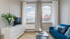 A modern living room with a blue sofa, white cabinet, and a TV on a stand. - Elite Apartments King Size Old Town (Gdansk)
