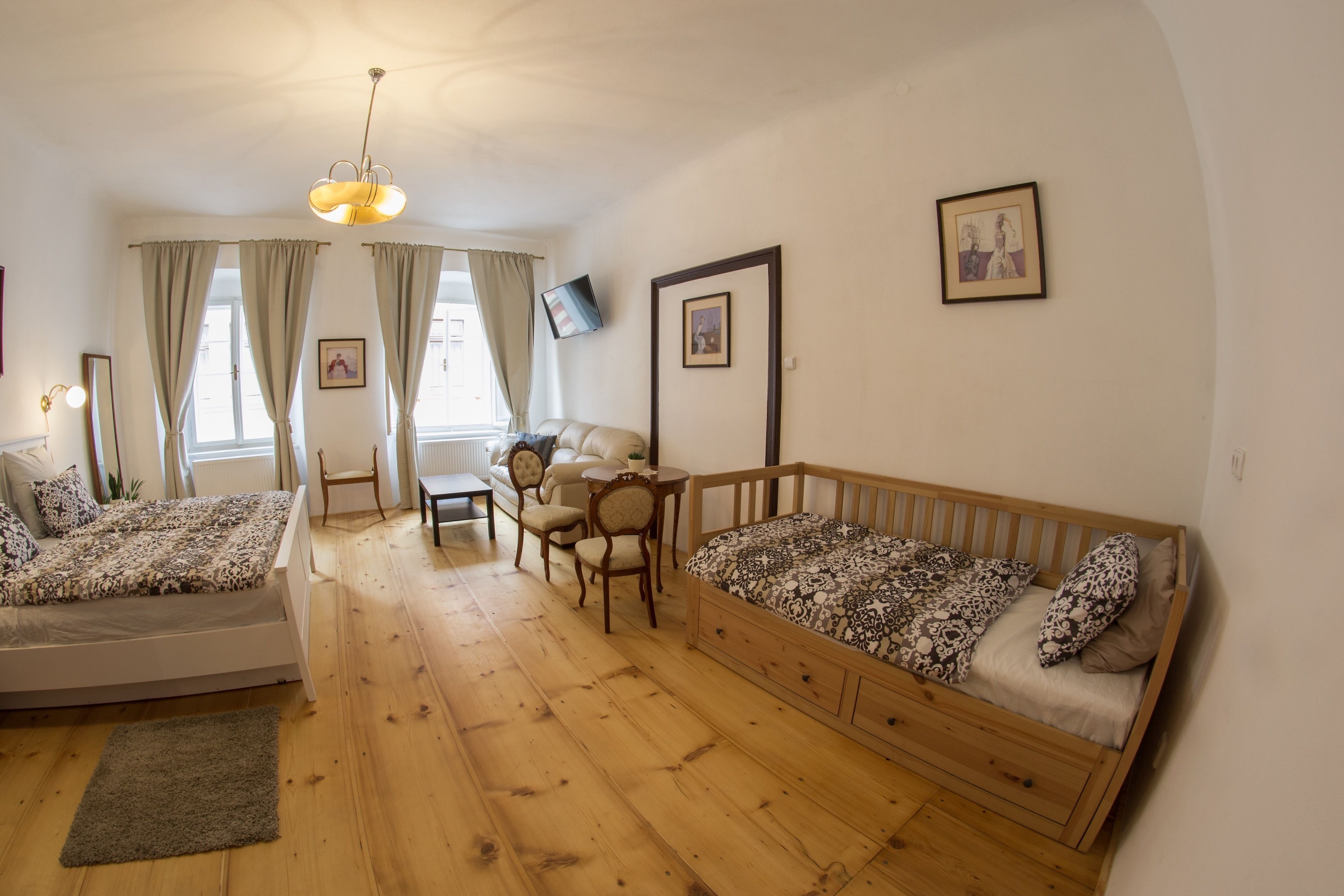 A cozy room with a bed, a sofa, a wooden floor, a table, and a chair.