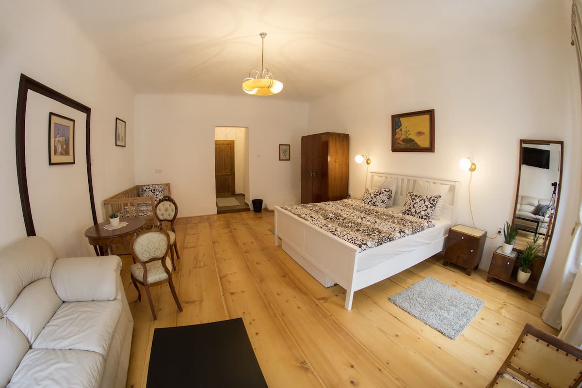 A bedroom with a bed, a chair, a small table, a wardrobe, and a mirror.