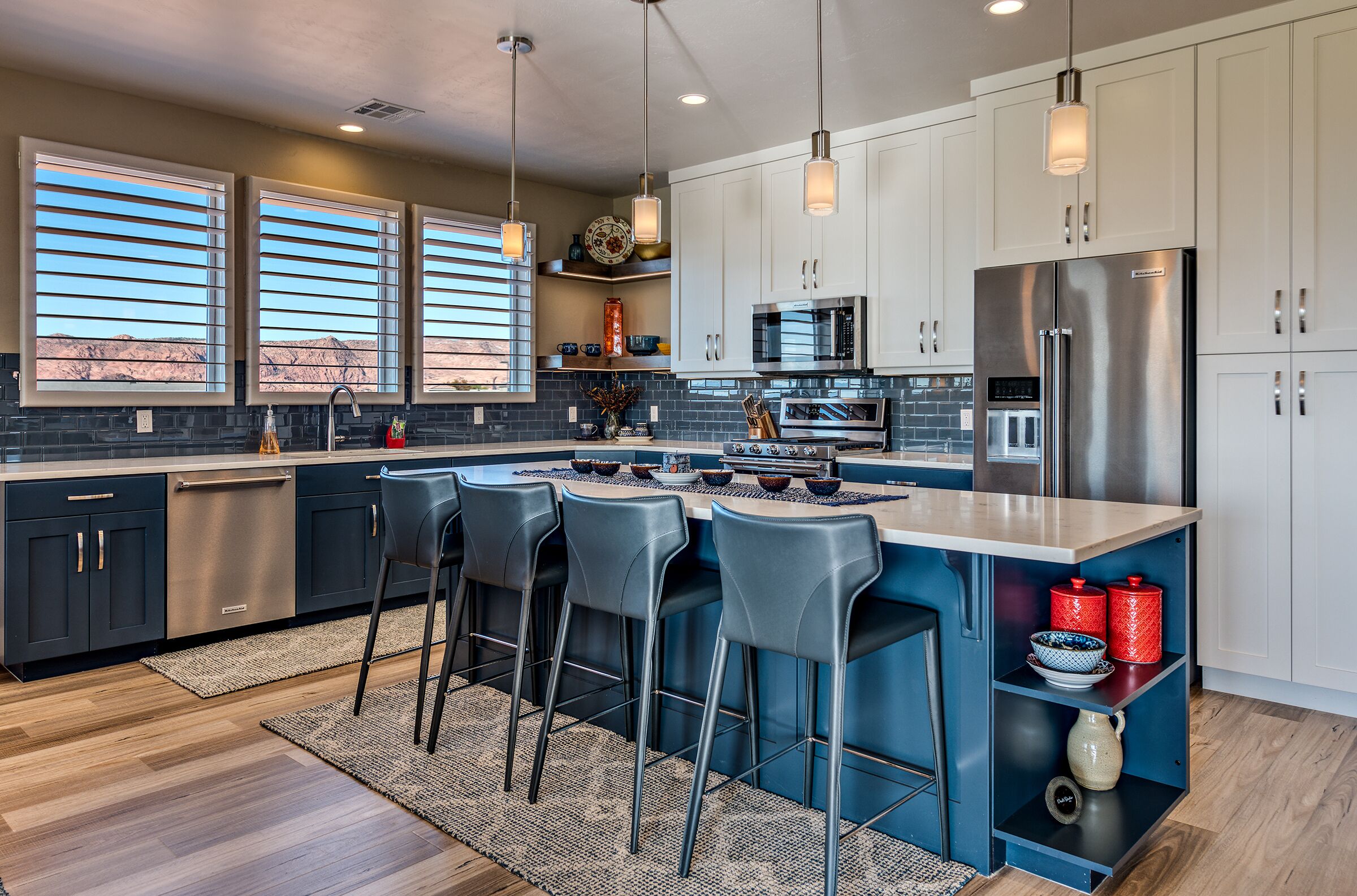 A modern kitchen with a central island, bar stools, stainless steel appliances, and a view of the desert through large windows.