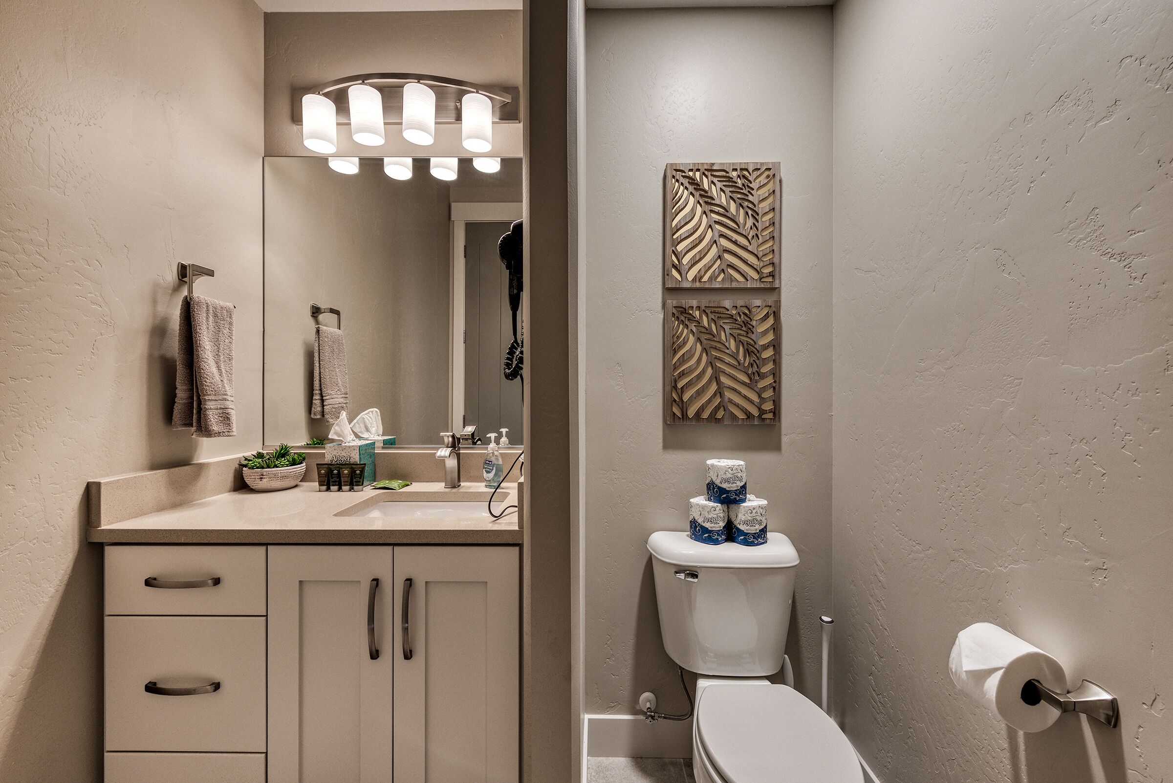 Een badkamer met toilet, wastafel en kastje. Handdoeken hangen aan de muur en er is een spiegel boven de wastafel.
