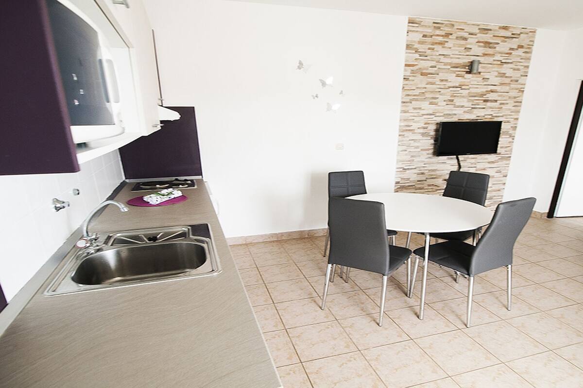 Una cocina compacta con fregadero, microondas y un pequeño comedor con sillas y una mesa.