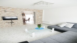 A modern living room with a stone wall, a flat-screen TV, a glass coffee table, a grey sofa, and a chandelier. - Villa Mona (Rogoznica)