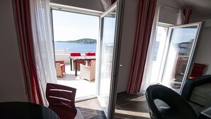 A room with a sliding glass door leading to an outdoor area with a table and chairs, and a view of the sea. - Villa Mona (Rogoznica)