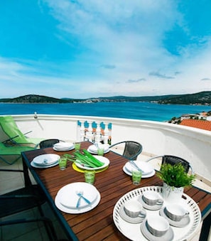 A dining table set for four on a boat with a view of the sea and distant land.