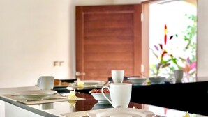 Uma sala de jantar com porta de madeira, mesa posta com pratos, copos e uma tigela de frutas.