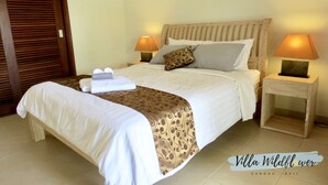 Uma cama bem arrumada com colcha estampada, duas luminárias de cabeceira e uma cabeceira de madeira.