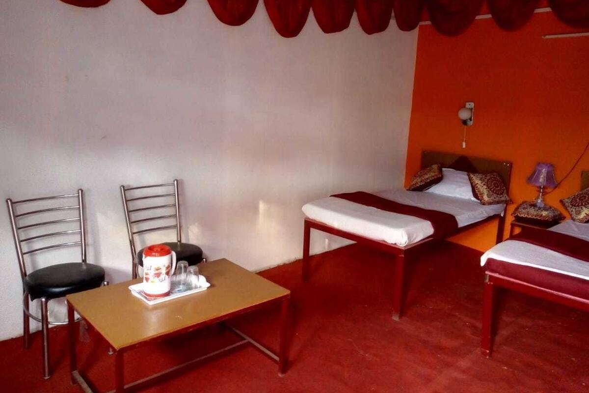 A room with two beds, a table with a kettle, and two chairs.