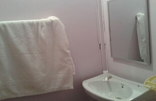 A bathroom with a white sink, a mirror, and a towel hanging on the wall.
