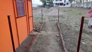Un sendero de tierra con bordes de ladrillo que conduce a un edificio con pared naranja y una celosía metálica en la ventana.
