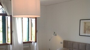 Ein Schlafzimmer mit einem großen Bett, einer Hängelampe, einem Nachttisch und einem Fenster mit Vorhängen.