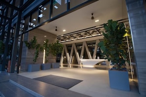 Welcome to our hotel lobby, featuring a spacious area with a central reception desk and large potted plants.