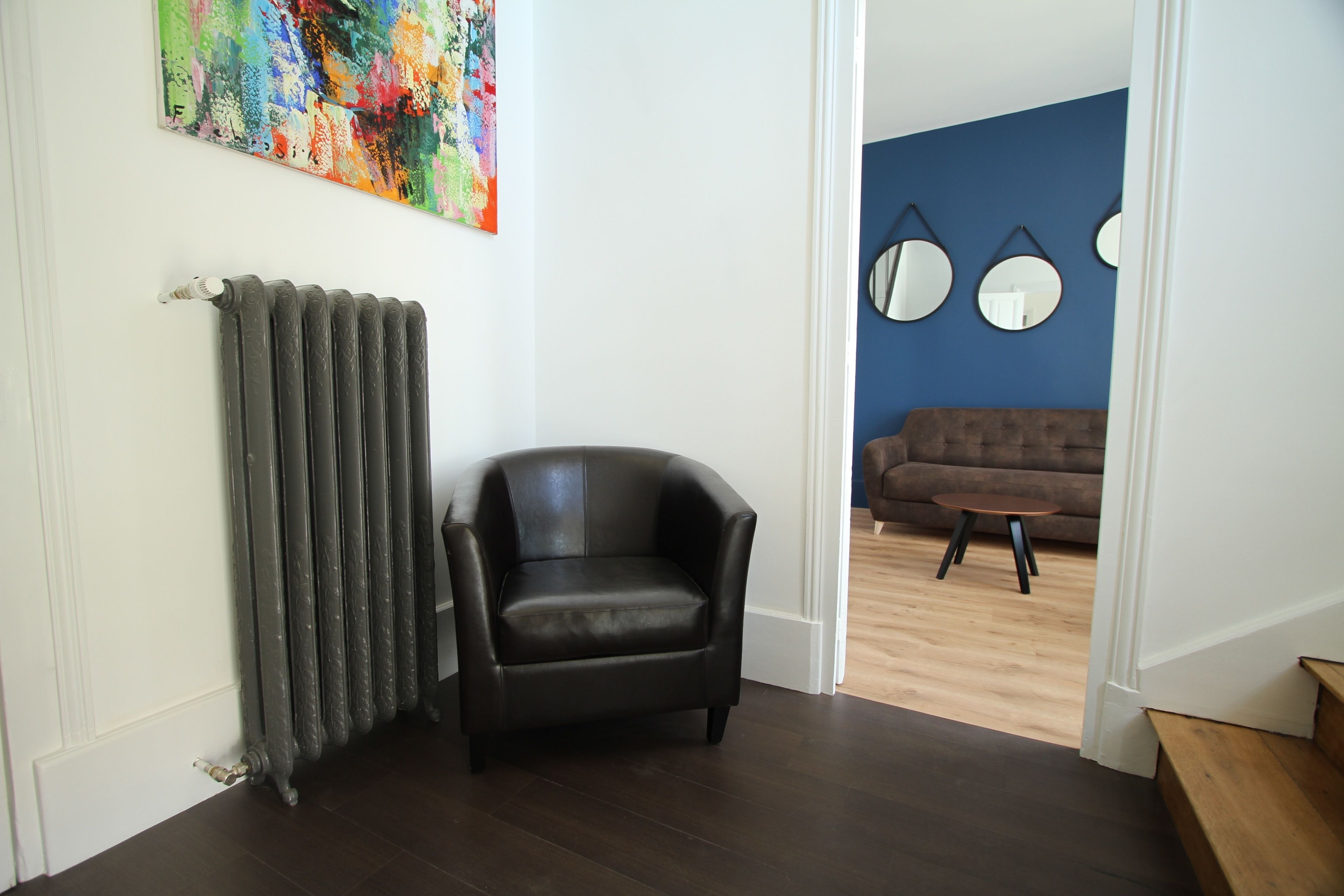 A room with a radiator, a black leather chair, and a blue wall with three round mirrors.