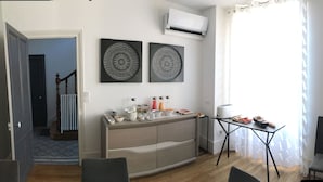 Una sala de estar moderna con comedor, que incluye un sofá, una mesa de centro y una mesa de comedor con un aparador. Hay dos unidades de aire acondicionado instaladas en la pared y dos piezas de decoración mural.