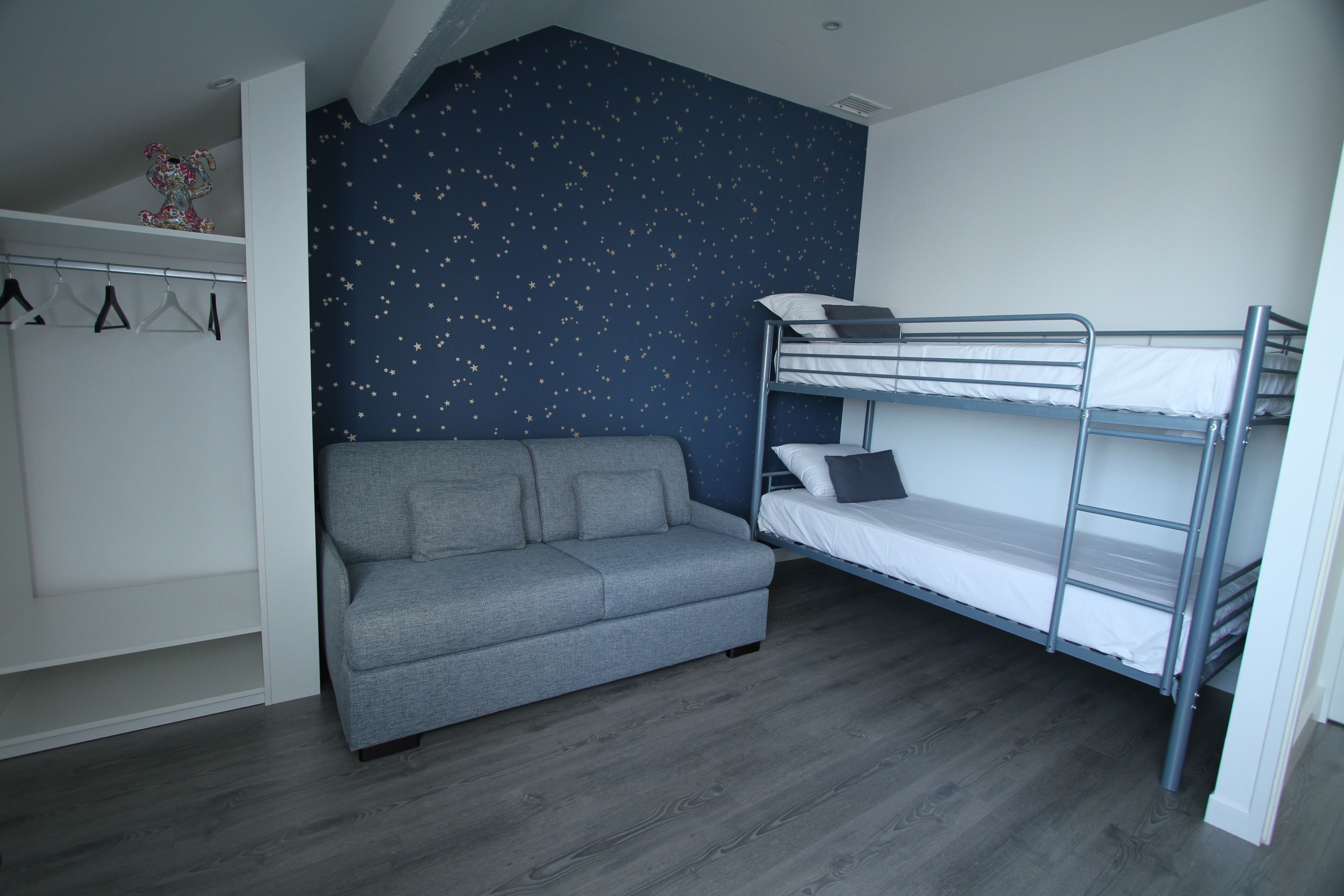 Una habitación con literas, un sofá gris y un armario.