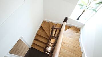 A wooden staircase with a handrail, white walls, and a window with a plant.