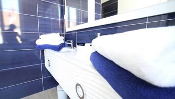 A modern bathroom with a white vanity, dark blue tiles, and a large mirror.