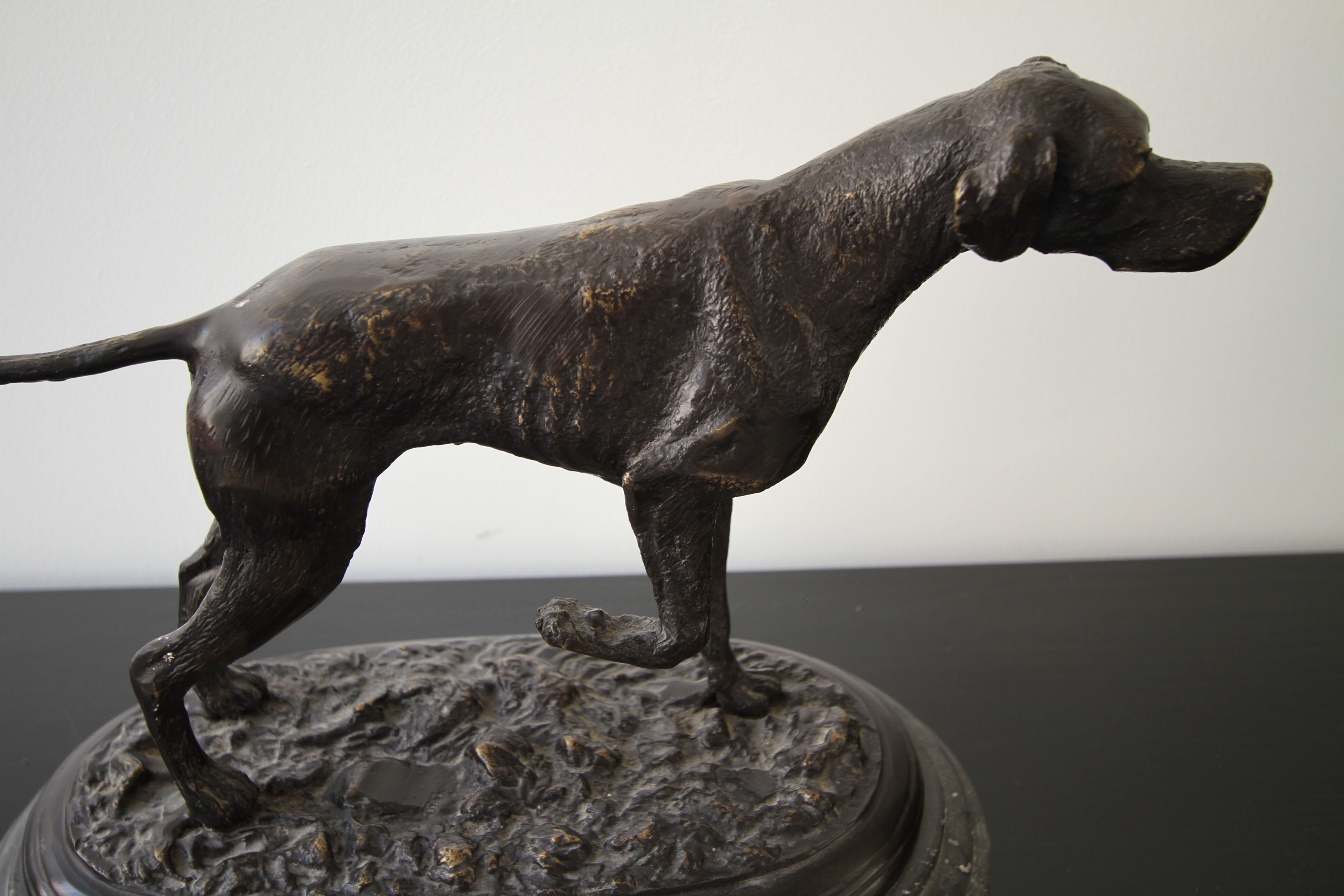Una estatua de bronce de un perro sobre un pedestal texturizado.
