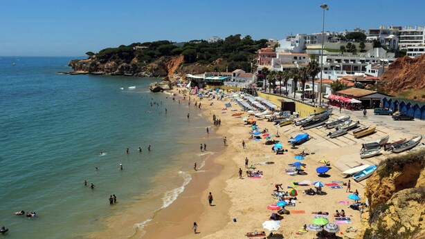 Una playa con gente, sombrillas y barcos.