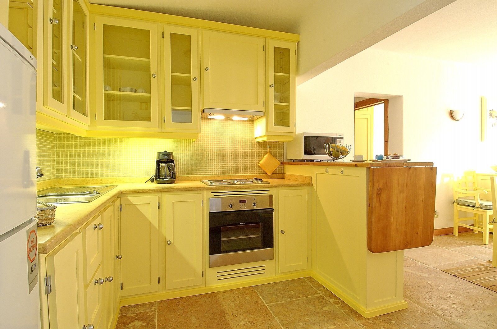 A compact kitchen with yellow cabinets, a built-in oven, and a microwave.