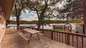 Une terrasse en pierre avec des tables de pique-nique donnant sur un lac, une clôture en bois et un petit pavillon.