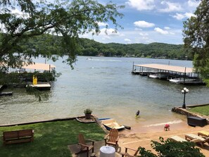 A lakeside view with a dock, a boat, and a grassy area with a bench and chairs.