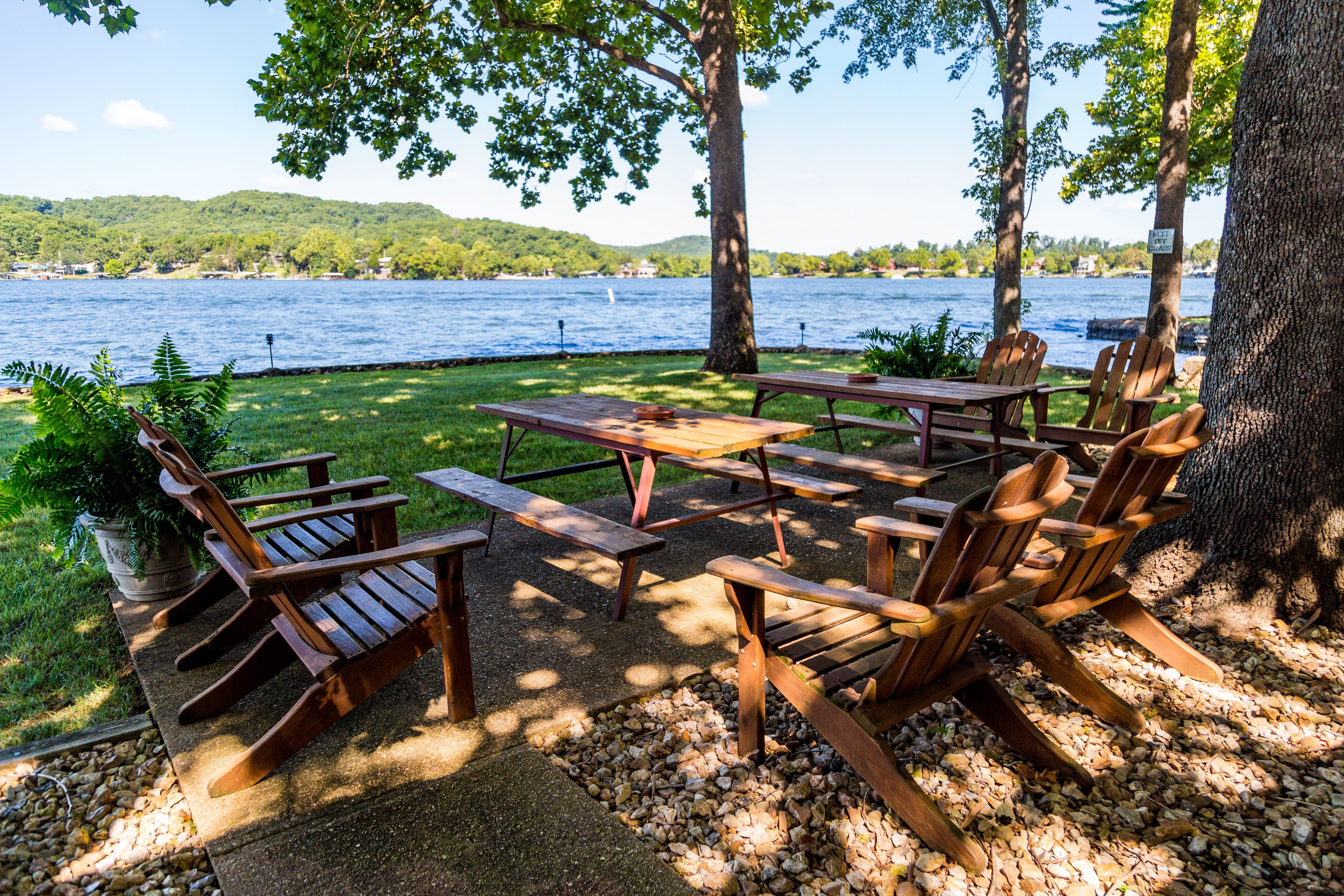 A lakeside picnic area with wooden benches and picnic tables, surrounded by trees and a view of the lake.