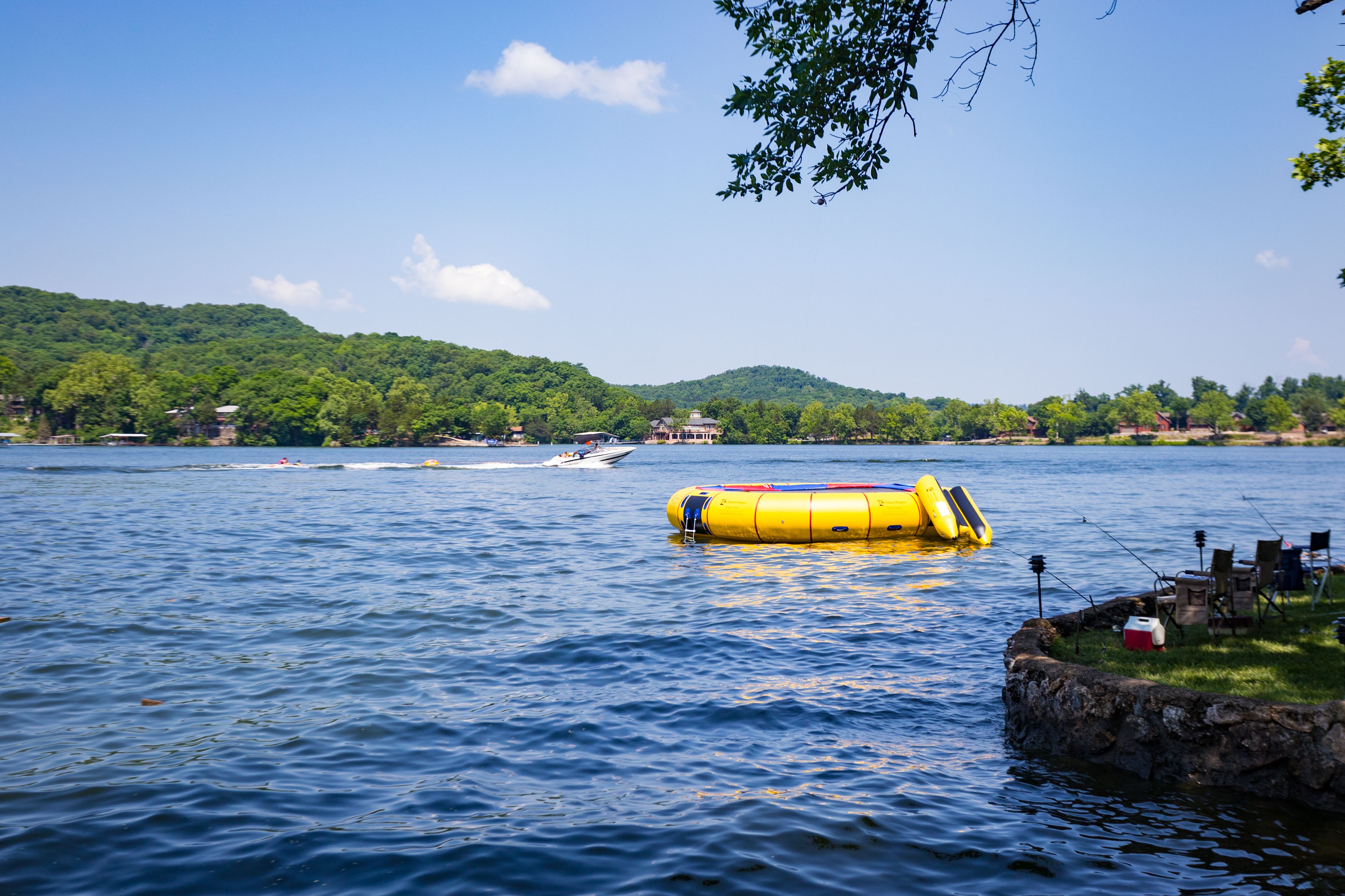A lake with a yellow floating platform, boats, and a house on a hill.