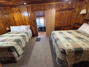 A room with wooden paneling, two beds with quilts, a door leading to another room, and a small table with chairs. - Point View Resort (Camdenton)