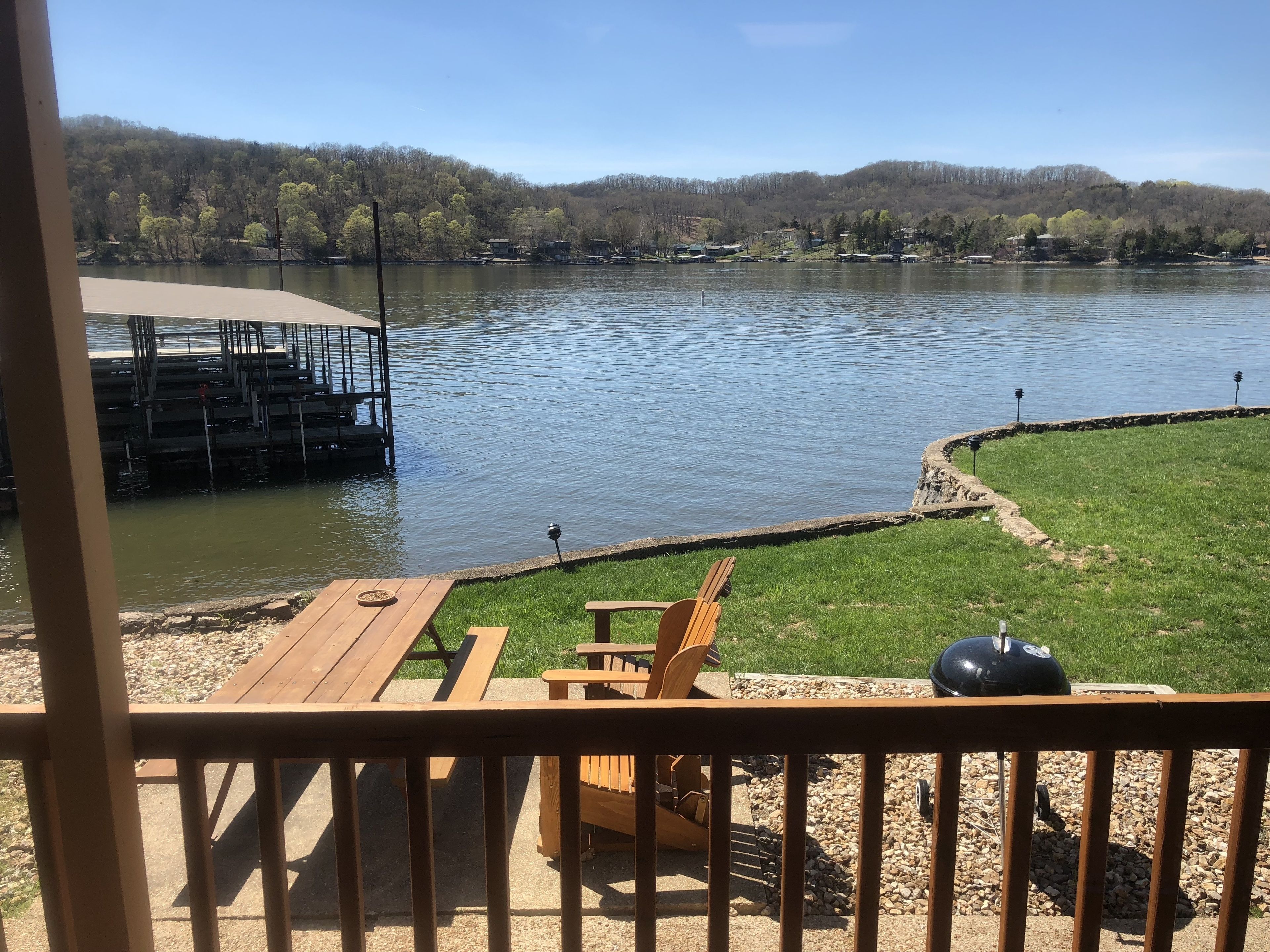 A deck with a view of a river, a grill, and a wooden chair.