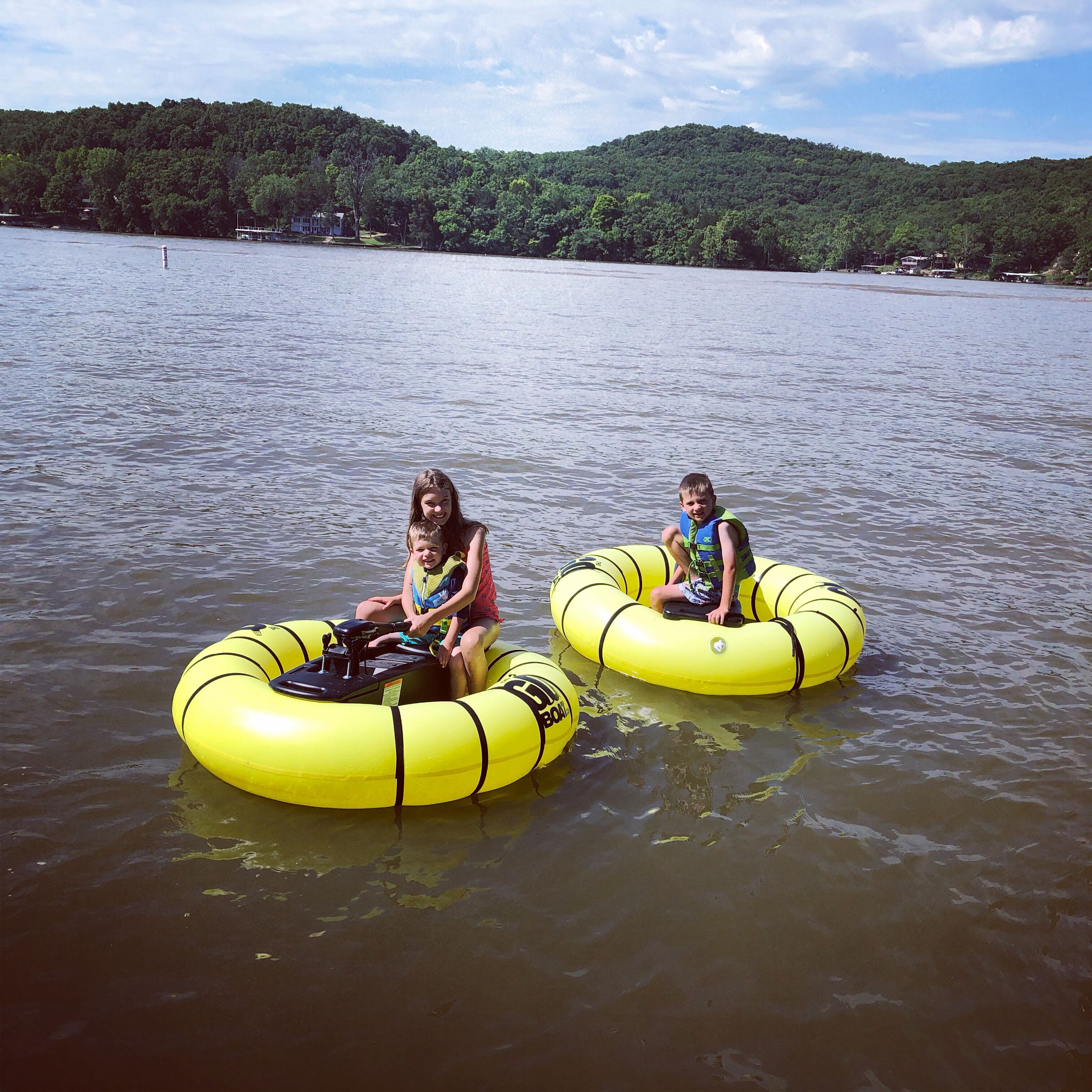 Two people on yellow inflatable tubes in a body of water with a forested hill in the background.