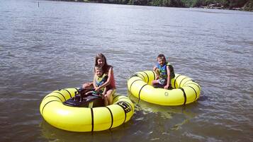 Two people on yellow inflatable tubes in a body of water with a forested hill in the background.