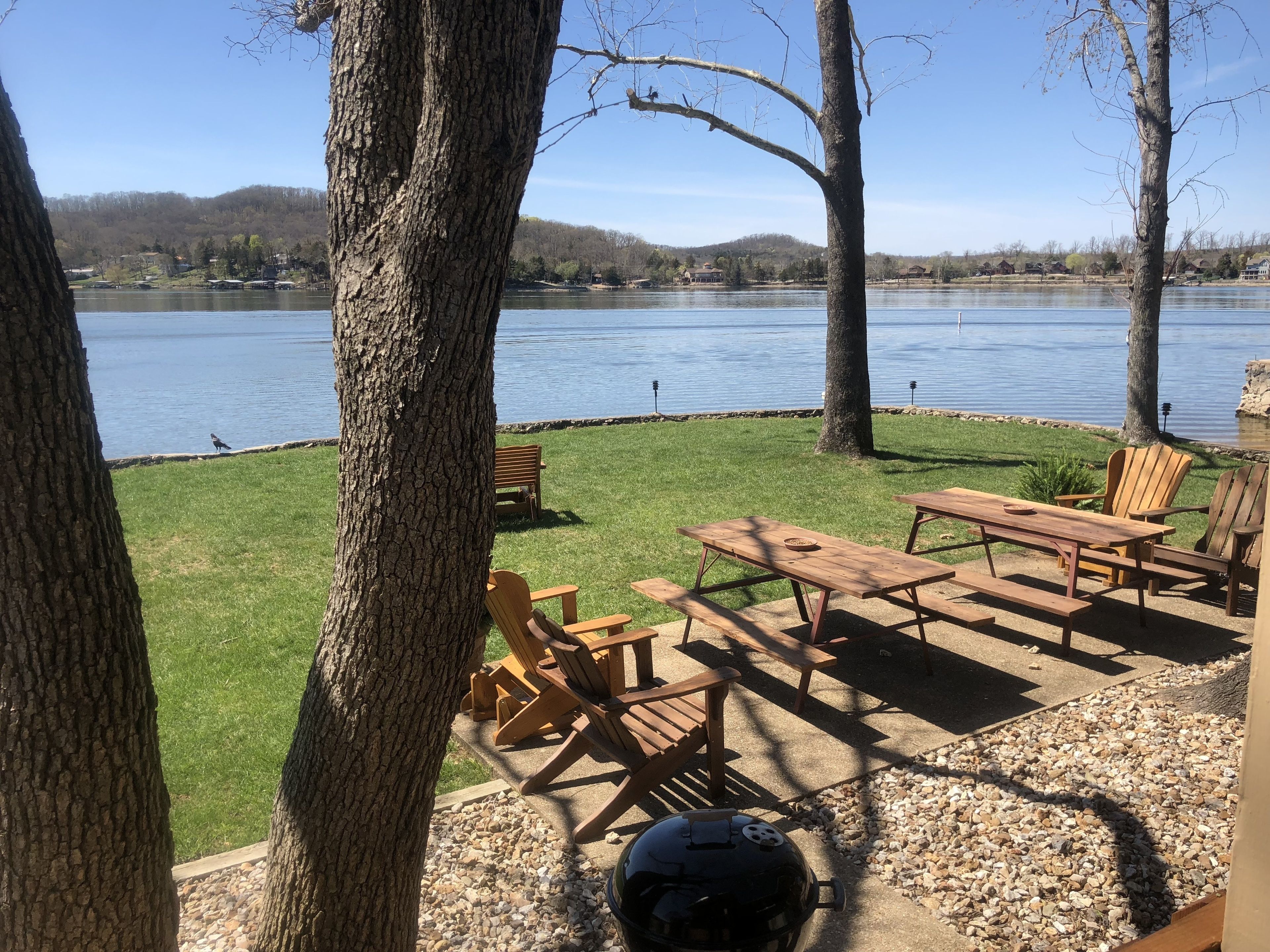 A lakeside patio with wooden furniture and a grill.