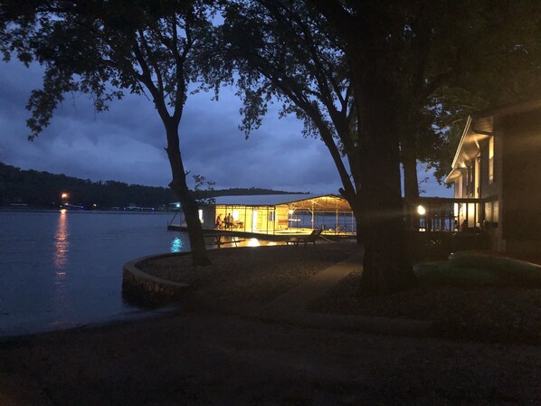 Una propiedad frente al lago con muelle, una zona cubierta con gente y una casa con porche.