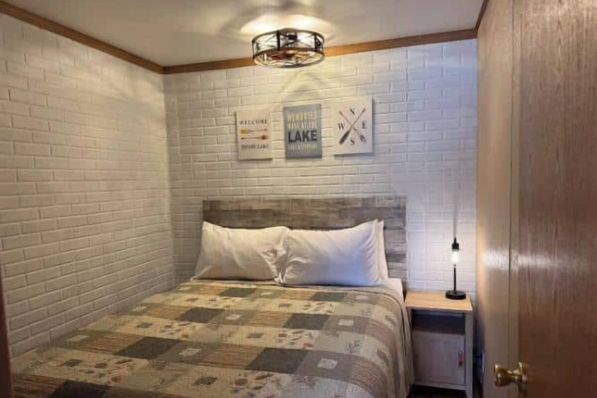 A bedroom with a quilted bedspread, a wooden headboard, a nightstand with a lamp, and a door.