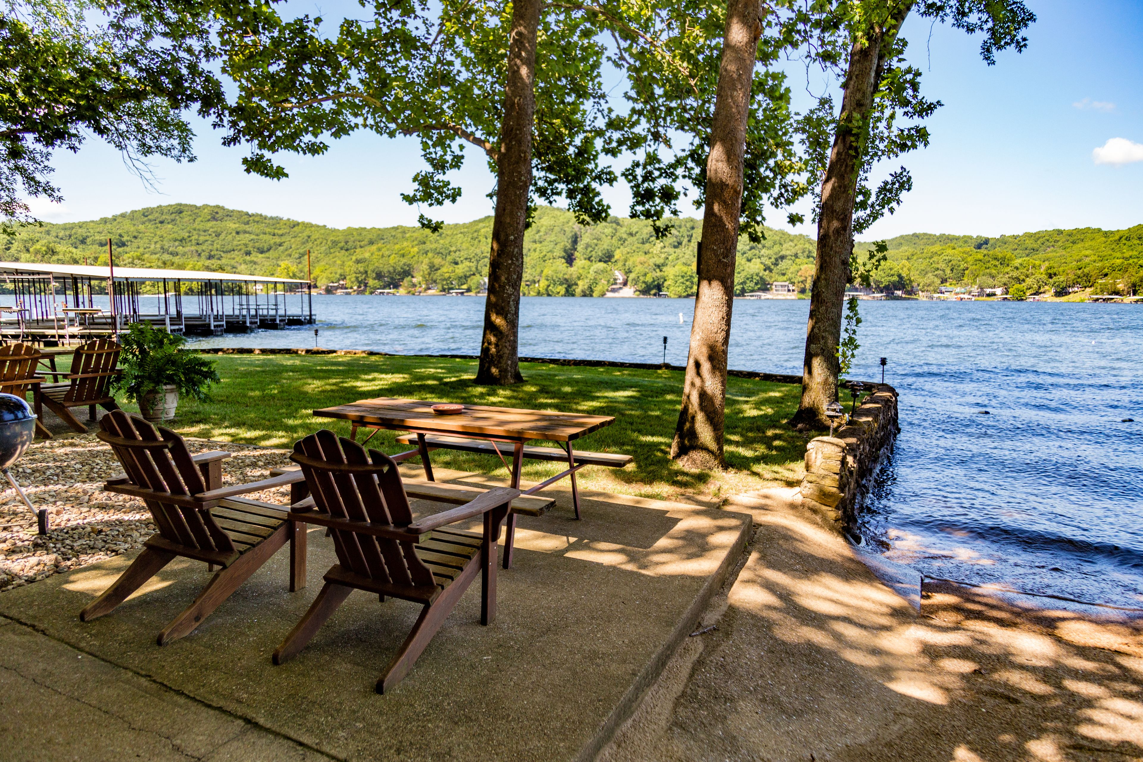 Une terrasse au bord du lac, avec des fauteuils Adirondack, une table de pique-nique et une jetée qui s’avance dans l’eau.