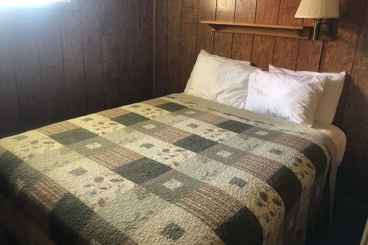 A bed with a quilt, a lamp, and wooden walls.