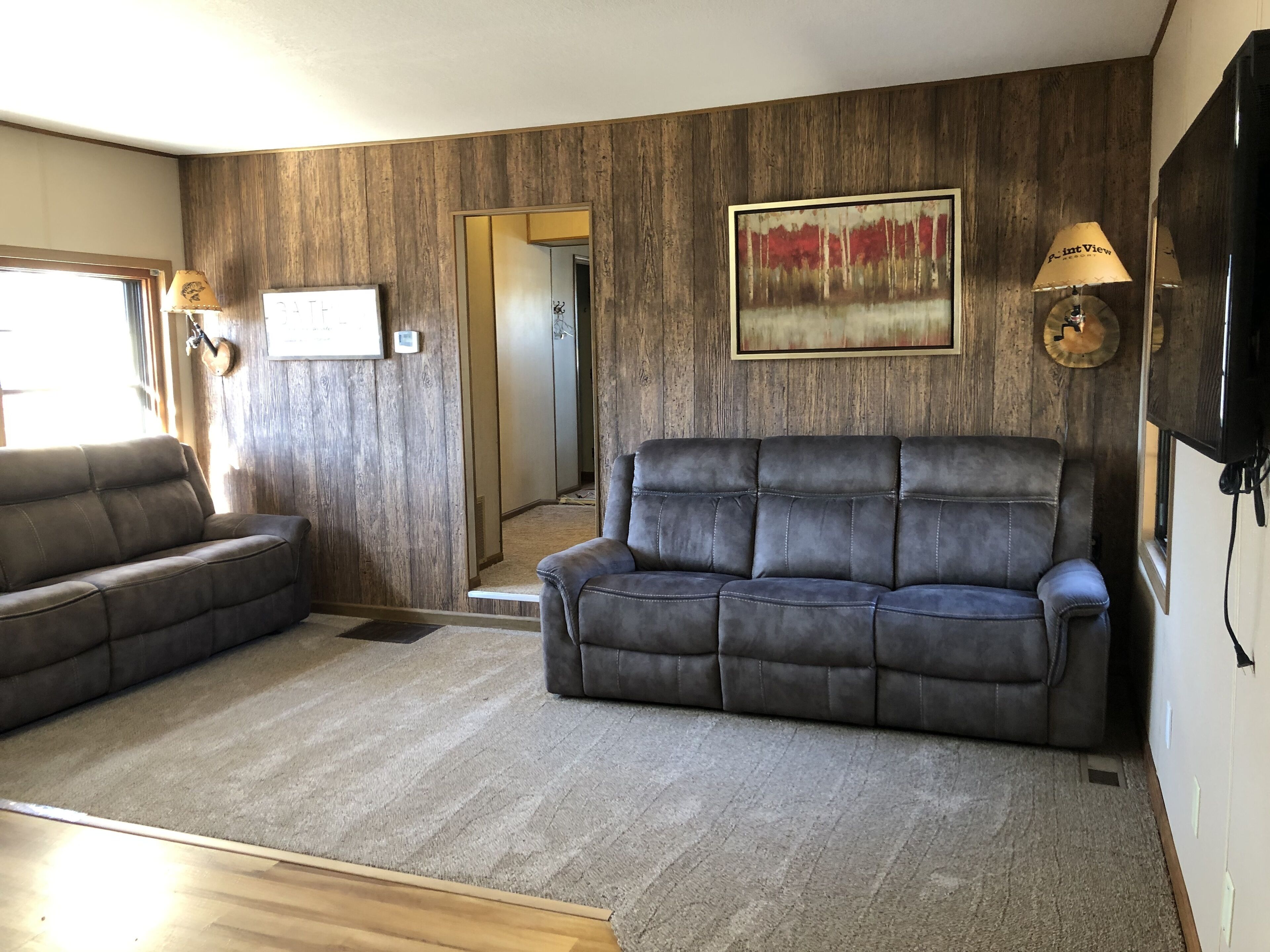 A living room with a wooden wall panel, two leather sofas, a rug, and a painting.